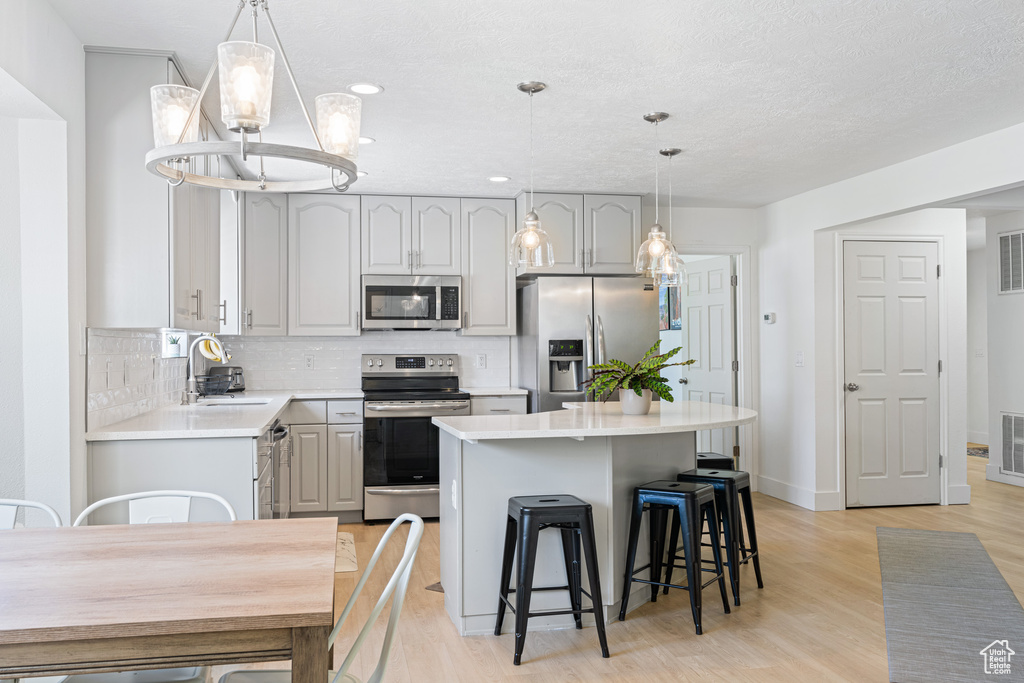 Kitchen featuring gray cabinetry, light hardwood / wood-style floors, stainless steel appliances, a center island, and sink