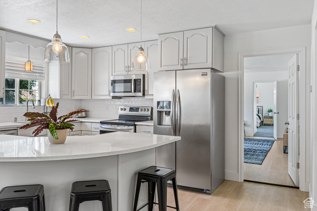 Kitchen featuring appliances with stainless steel finishes, light hardwood / wood-style floors, light stone countertops, and pendant lighting