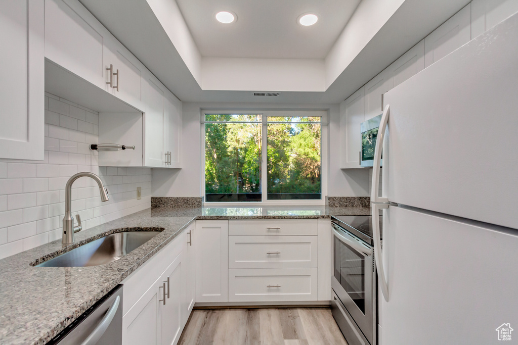 Kitchen with light stone counters, sink, white cabinetry, stainless steel appliances, and light hardwood / wood-style floors