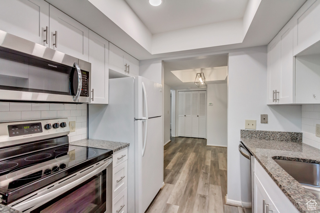 Kitchen featuring light wood-type flooring, white cabinetry, appliances with stainless steel finishes, light stone countertops, and decorative backsplash