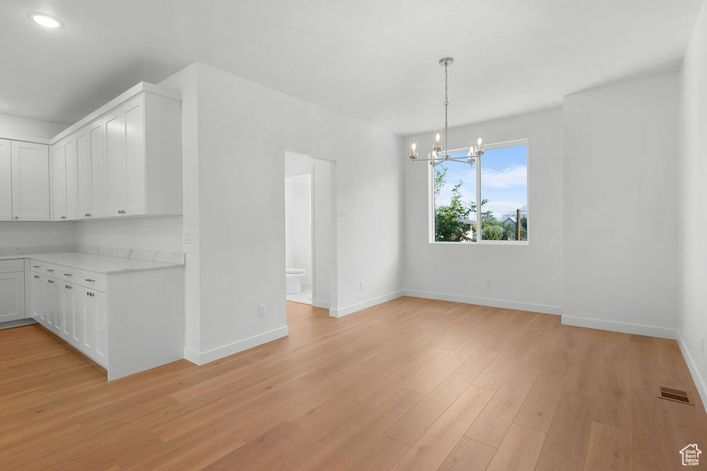 Kitchen with pendant lighting, an inviting chandelier, light hardwood / wood-style flooring, and white cabinetry