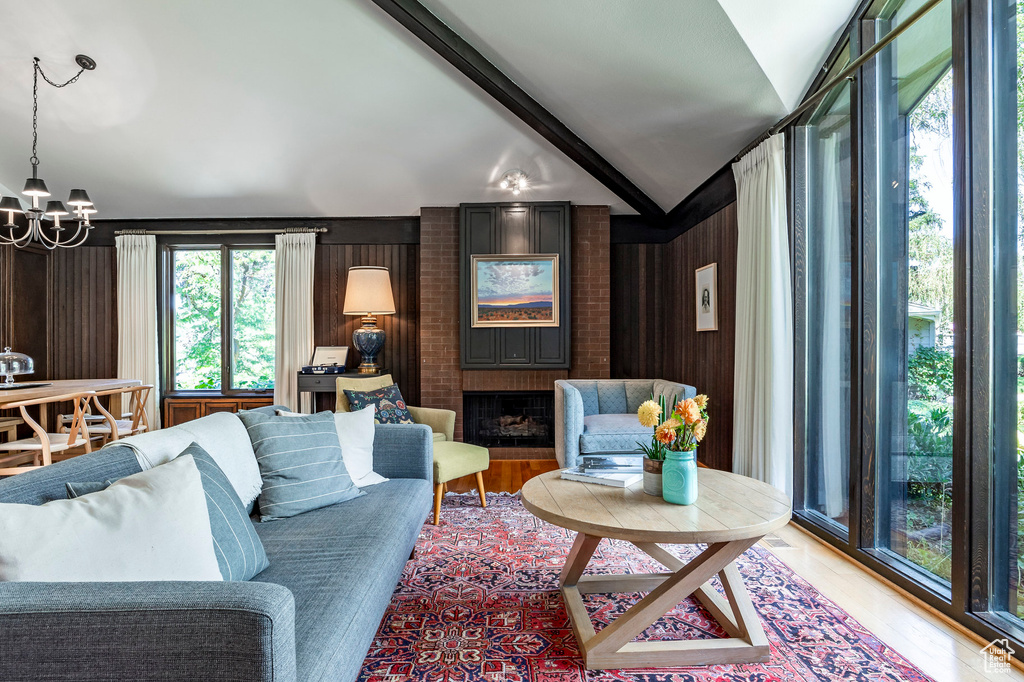 Living room with vaulted ceiling with beams, wooden walls, light hardwood / wood-style floors, and a chandelier