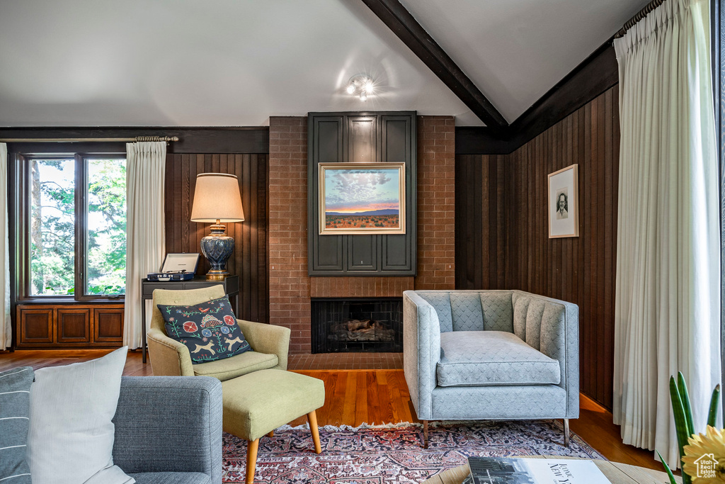 Sitting room featuring lofted ceiling with beams, a brick fireplace, wood-type flooring, and wooden walls