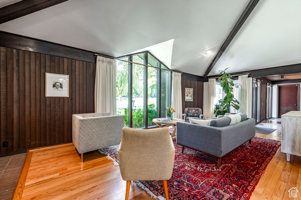 Living room with lofted ceiling with beams, wooden walls, hardwood / wood-style flooring, and floor to ceiling windows