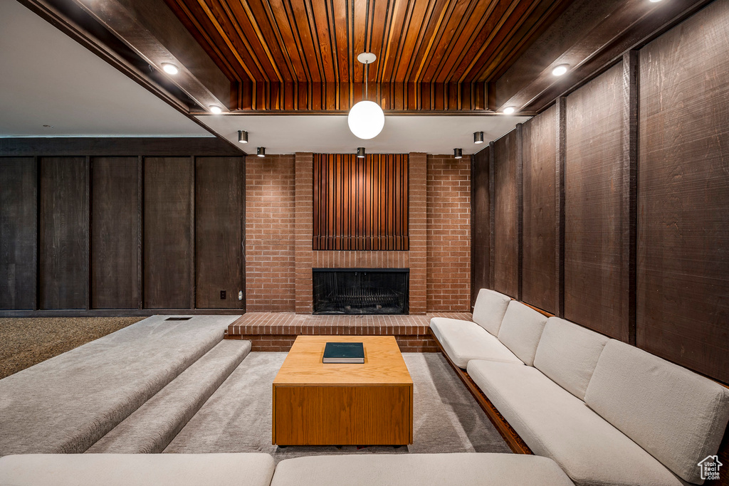 Carpeted living room featuring a brick fireplace, wooden walls, and wood ceiling