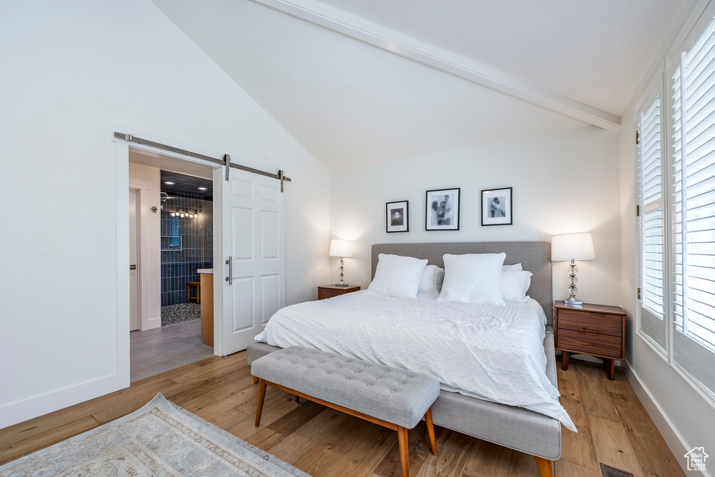 Bedroom with a barn door, vaulted ceiling with beams, and light hardwood / wood-style flooring