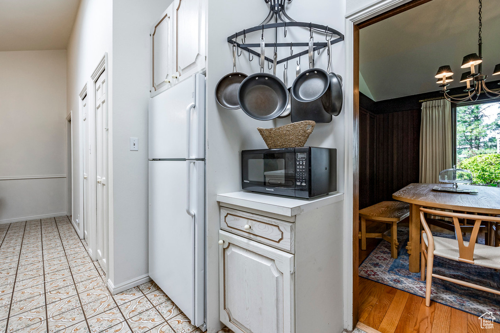 Kitchen featuring a notable chandelier, white cabinets, lofted ceiling, and white fridge