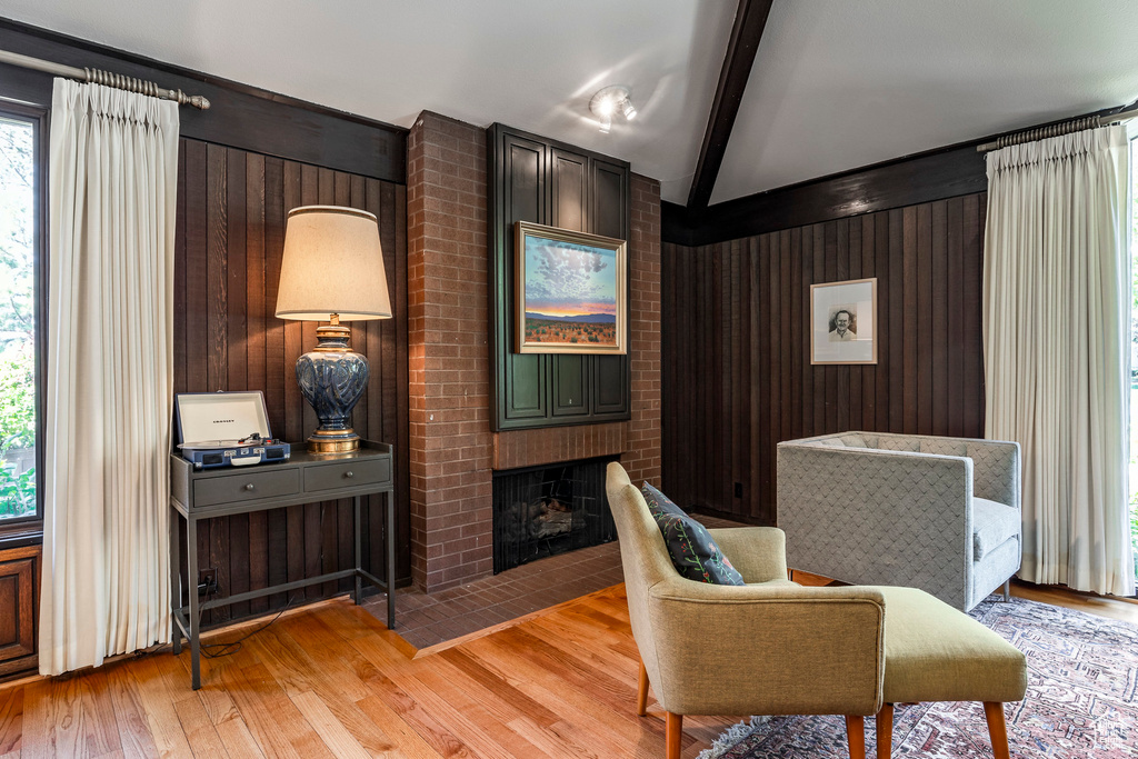 Interior space with vaulted ceiling with beams, light hardwood / wood-style floors, wood walls, and a fireplace