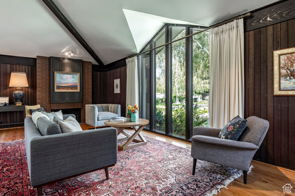 Living room featuring wooden walls, light hardwood / wood-style flooring, lofted ceiling with beams, and a wealth of natural light