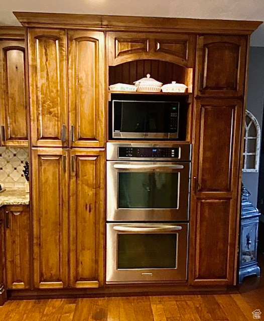 Kitchen with light stone counters, appliances with stainless steel finishes, dark hardwood / wood-style flooring, and decorative backsplash