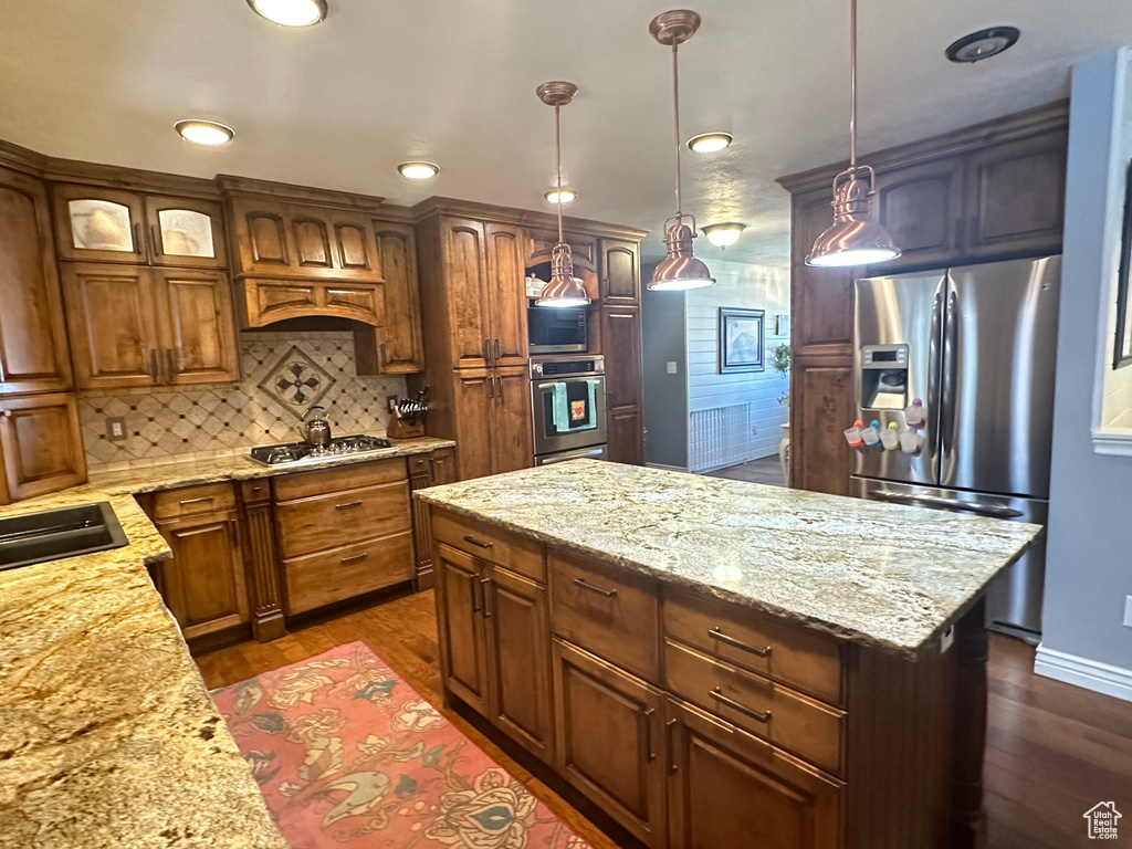 Kitchen with a kitchen island, decorative light fixtures, stainless steel appliances, dark hardwood / wood-style floors, and decorative backsplash