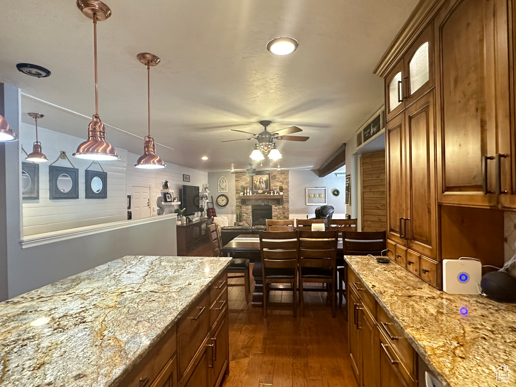 Kitchen featuring light stone countertops, a stone fireplace, dark wood-type flooring, and ceiling fan