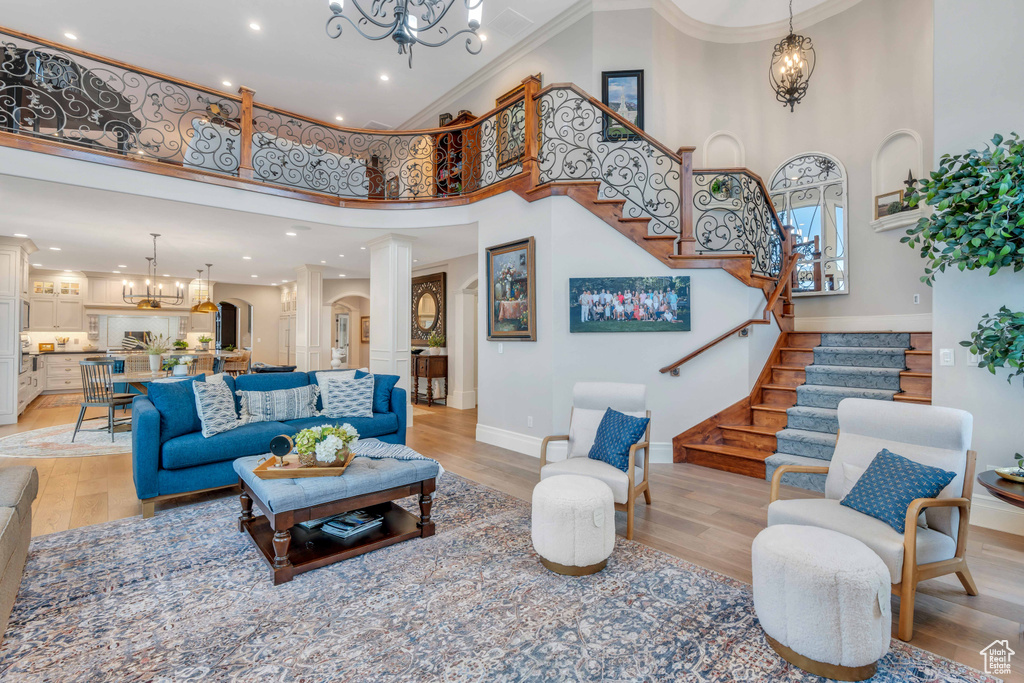 Living room featuring ornamental molding, a high ceiling, a chandelier, and light wood-type flooring