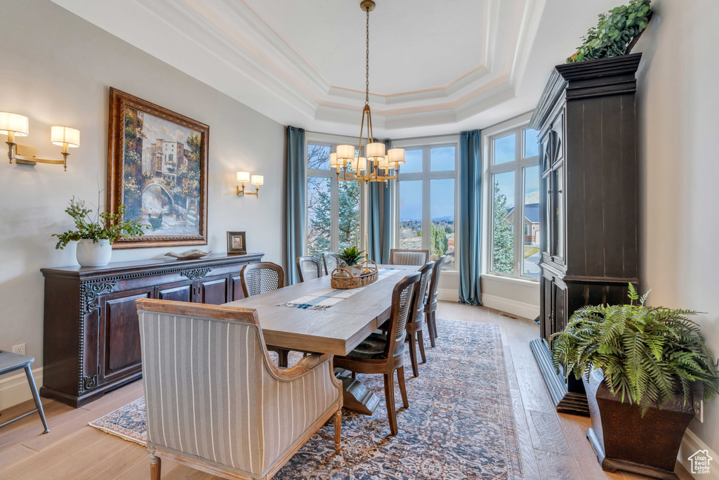 Dining space with ornamental molding, a notable chandelier, a tray ceiling, and light hardwood / wood-style floors