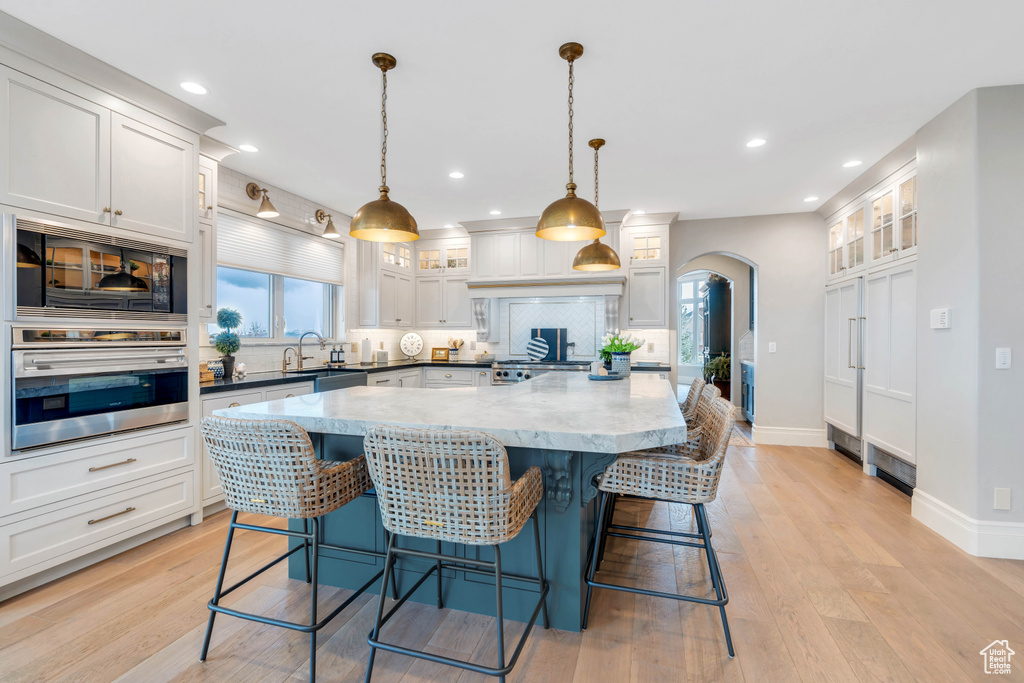 Kitchen featuring white cabinets, pendant lighting, stainless steel appliances, light wood-type flooring, and a kitchen bar