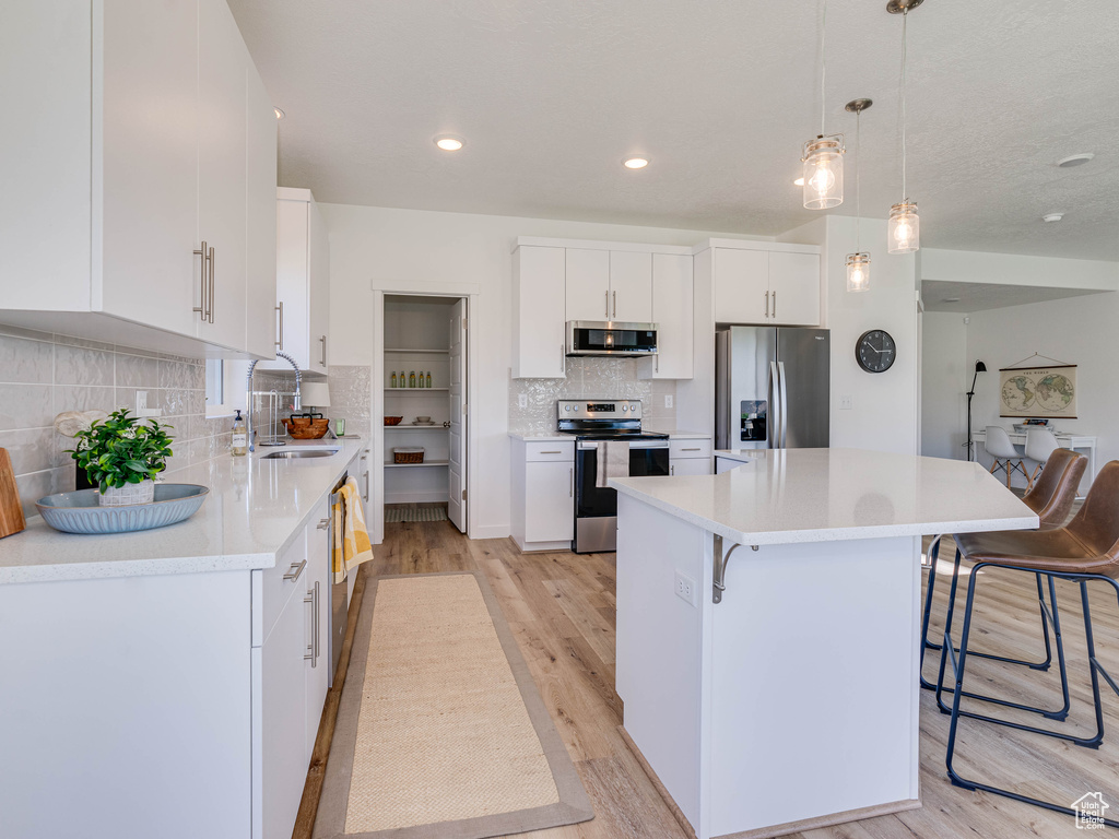 Kitchen featuring light hardwood / wood-style flooring, white cabinetry, appliances with stainless steel finishes, and a center island