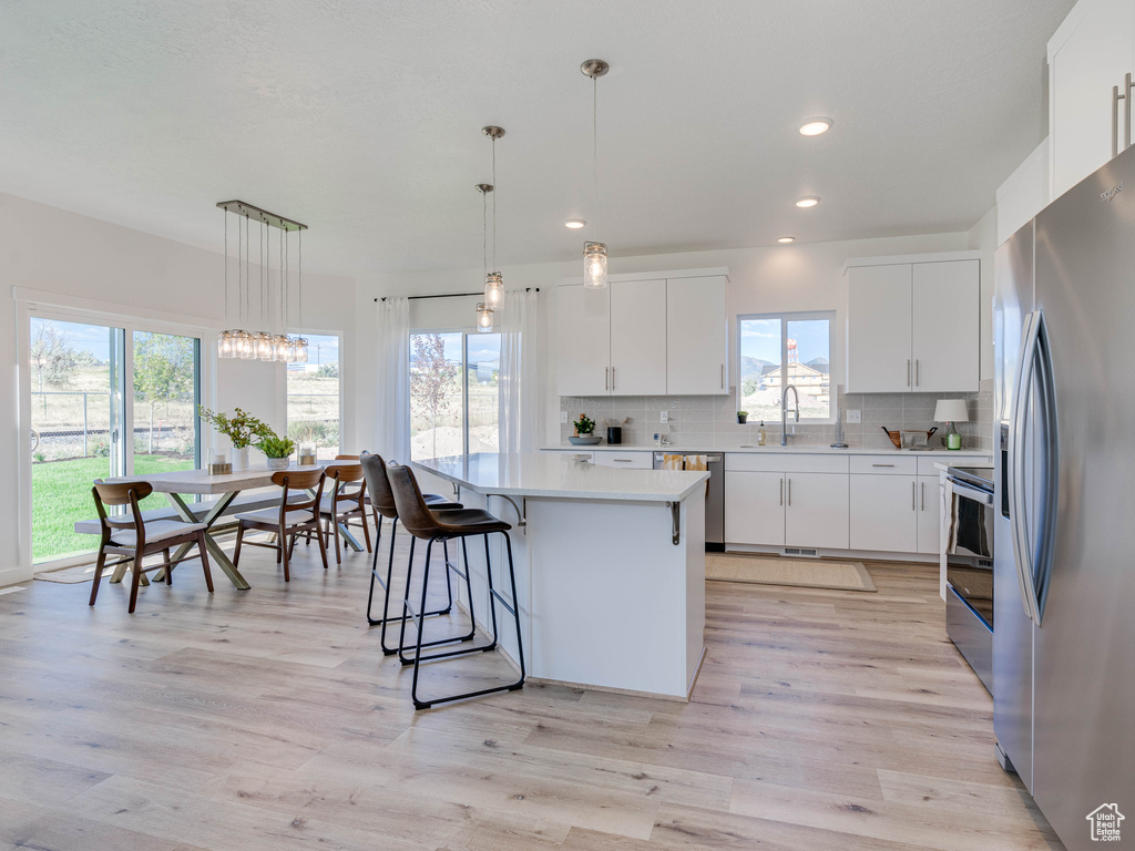 Kitchen featuring appliances with stainless steel finishes, hanging light fixtures, light hardwood / wood-style flooring, and white cabinets