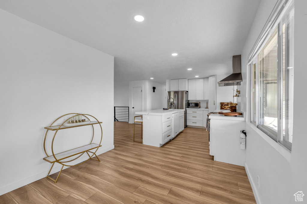 Kitchen featuring white cabinets, wall chimney range hood, stainless steel appliances, a center island, and light wood-type flooring