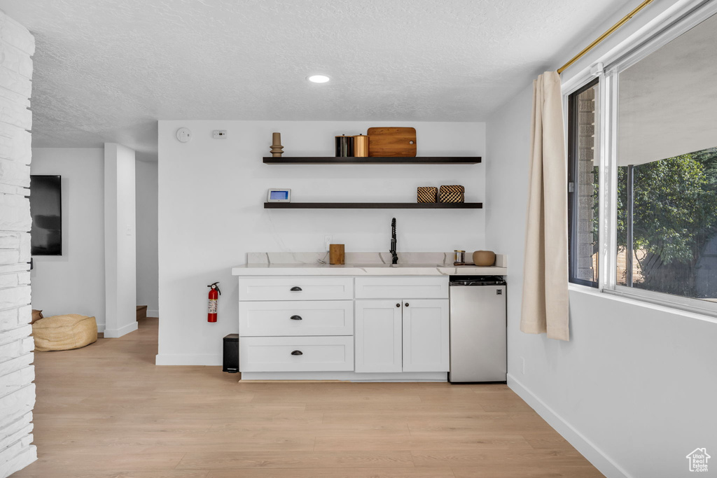 Bar with light hardwood / wood-style floors, white cabinets, dishwasher, a textured ceiling, and sink