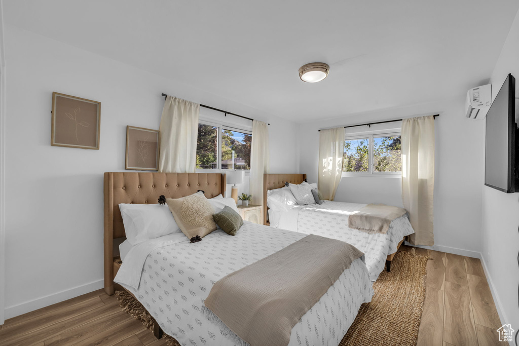 Bedroom with an AC wall unit, multiple windows, and hardwood / wood-style flooring