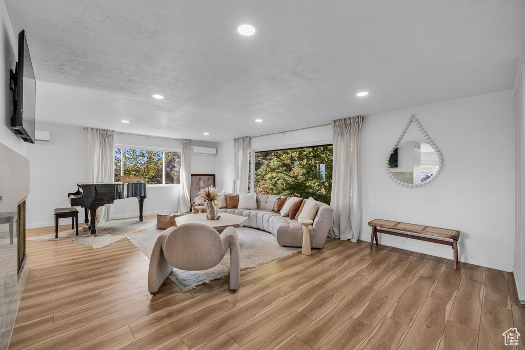 Living room with a textured ceiling, light hardwood / wood-style floors, and a wall unit AC