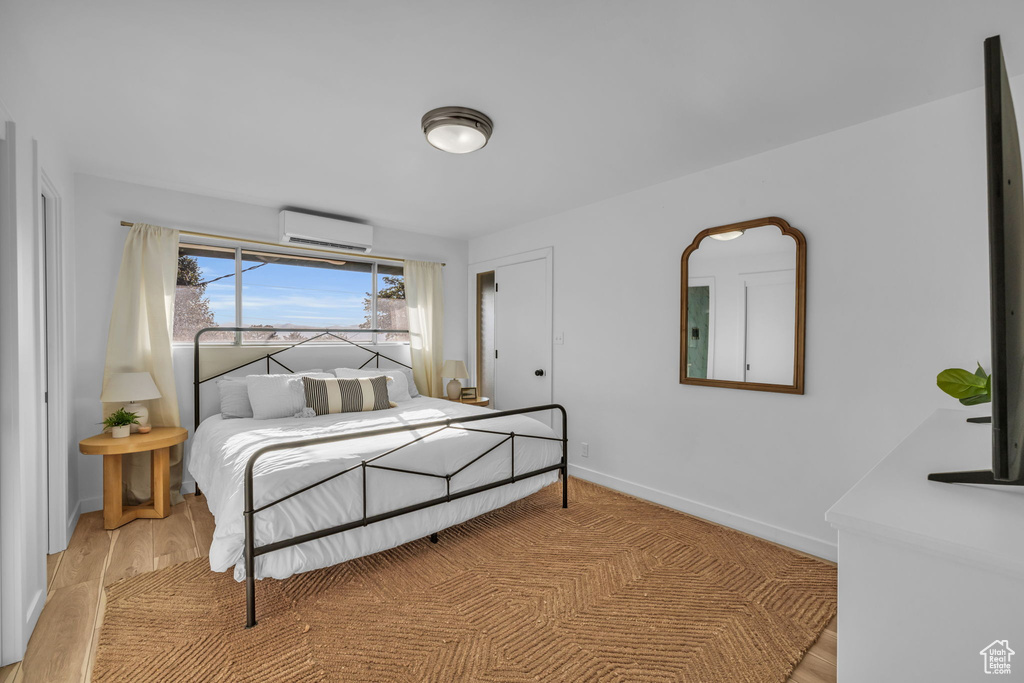 Bedroom with light hardwood / wood-style floors and an AC wall unit