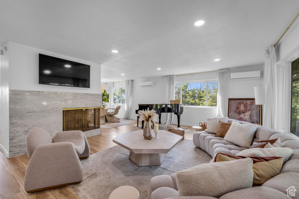 Living room with light hardwood / wood-style floors, an AC wall unit, and a premium fireplace