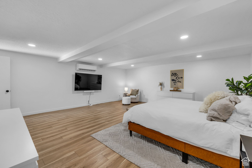 Bedroom featuring beamed ceiling, an AC wall unit, and light hardwood / wood-style flooring