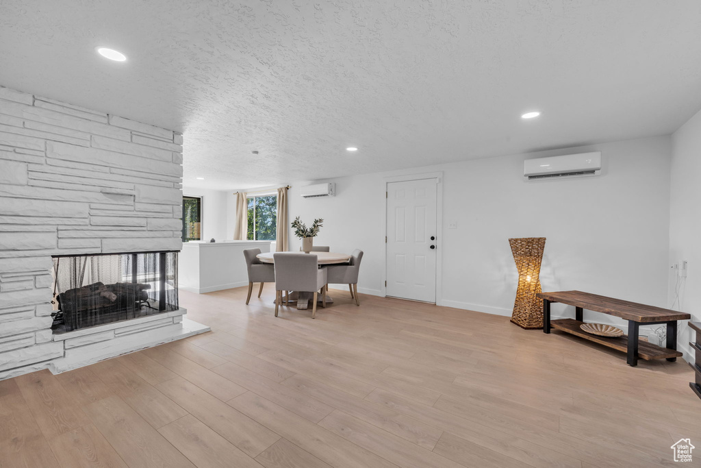 Living room featuring an AC wall unit, light wood-type flooring, a textured ceiling, and a stone fireplace