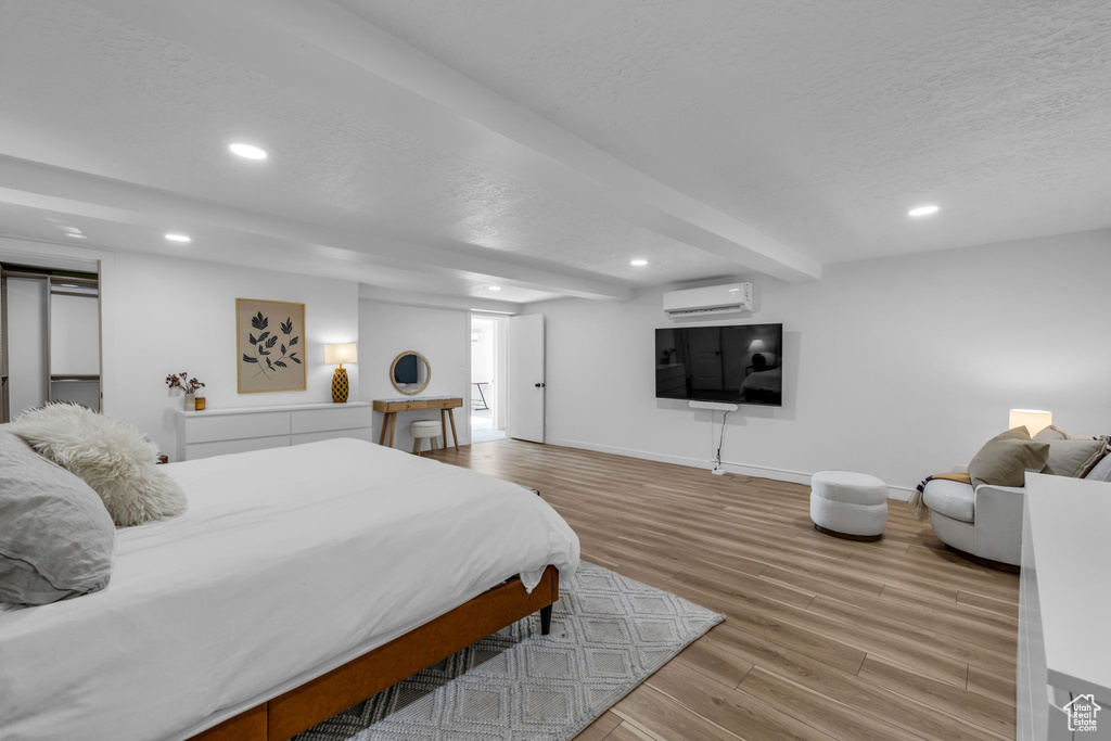 Bedroom featuring an AC wall unit, light hardwood / wood-style floors, and a textured ceiling