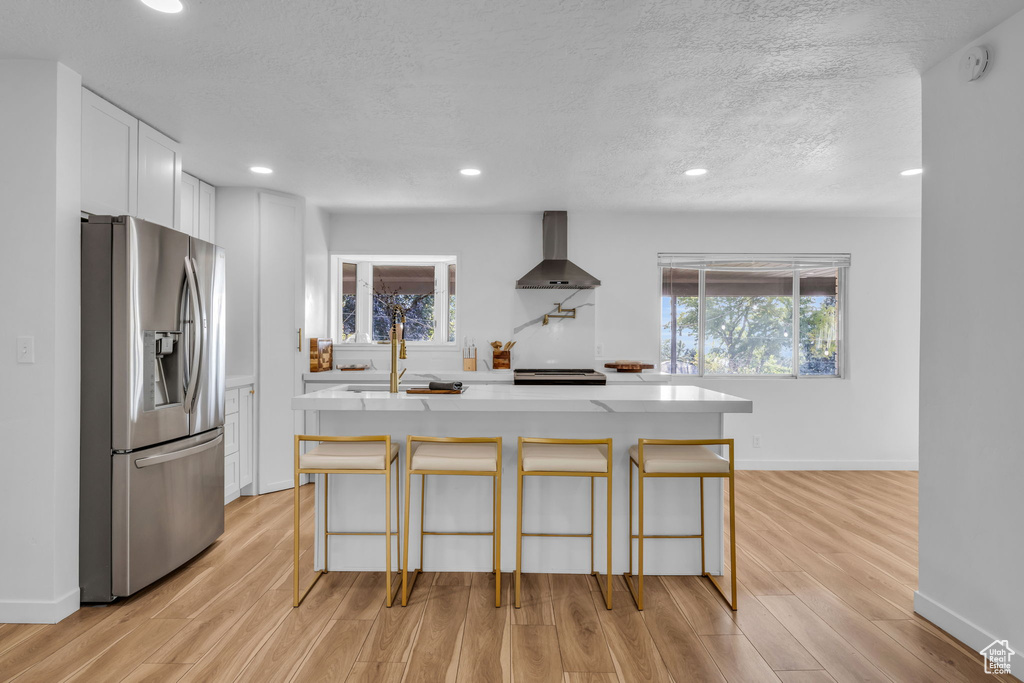 Kitchen featuring light wood-type flooring, white cabinets, wall chimney range hood, a kitchen breakfast bar, and stainless steel appliances