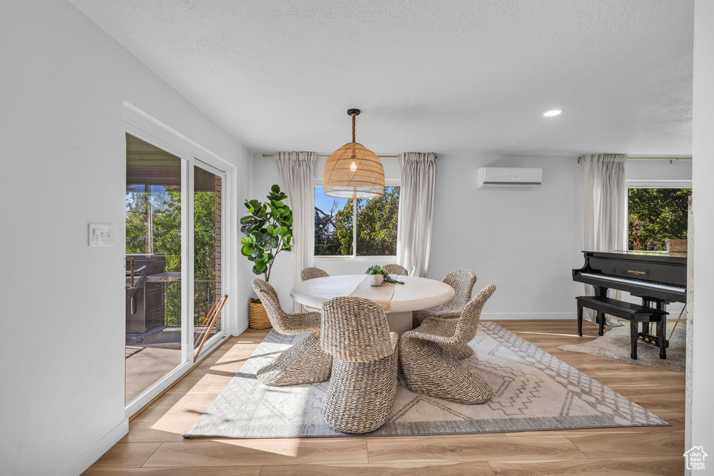 Dining space featuring light wood-type flooring, a textured ceiling, and a wall mounted air conditioner