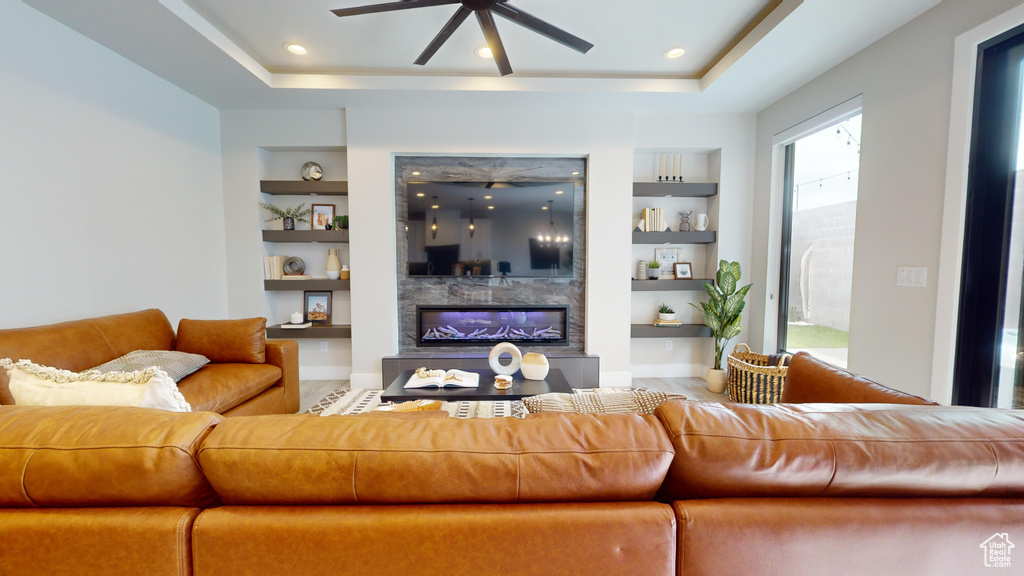 Living room featuring built in shelves, a high end fireplace, ceiling fan, and a raised ceiling