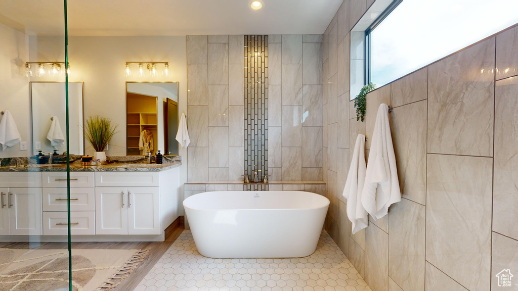 Bathroom featuring tile walls, tile patterned flooring, a bath, and vanity