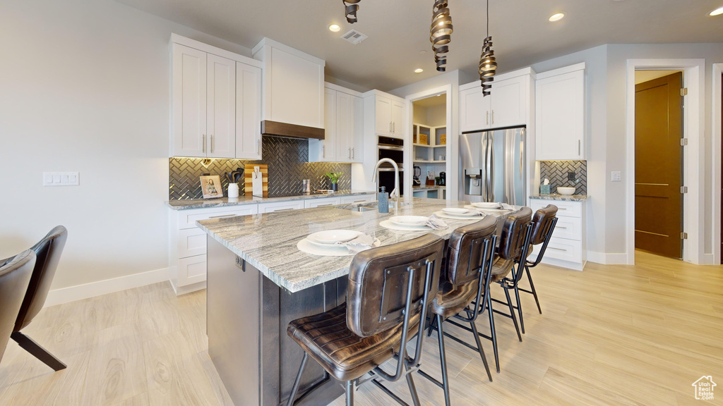 Kitchen with light stone counters, a kitchen island with sink, white cabinets, light hardwood / wood-style flooring, and stainless steel appliances