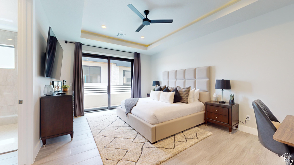 Bedroom featuring light hardwood / wood-style floors, multiple windows, a raised ceiling, and access to exterior