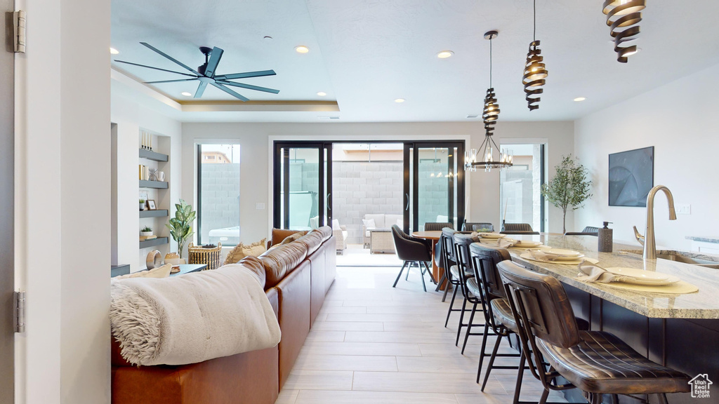 Living room with built in shelves, sink, light hardwood / wood-style flooring, a tray ceiling, and ceiling fan with notable chandelier