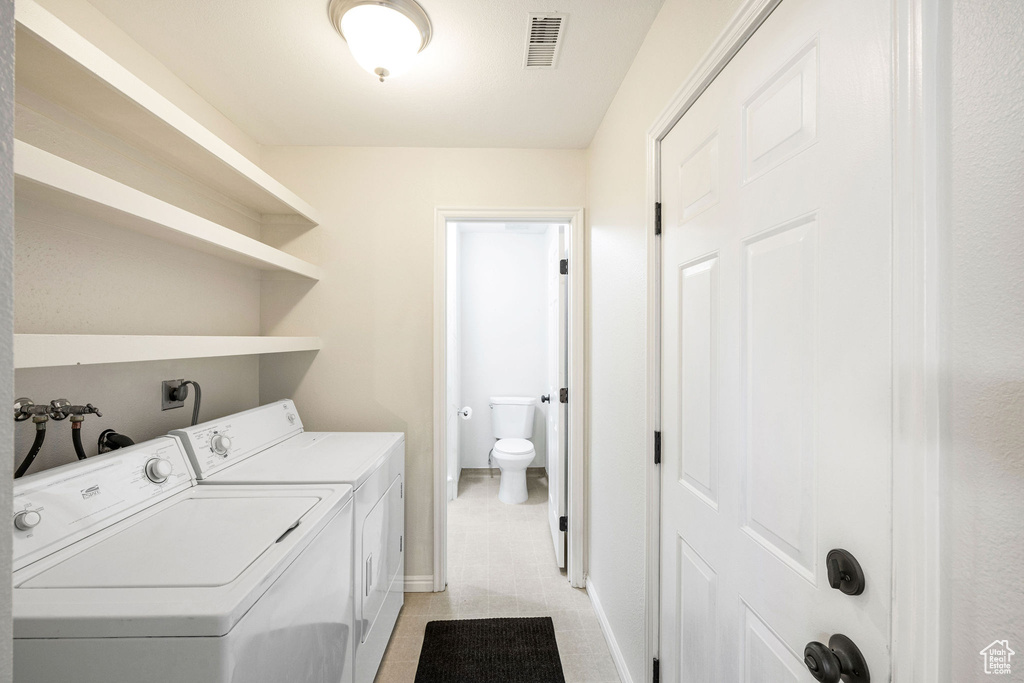 Clothes washing area with light tile patterned floors and separate washer and dryer