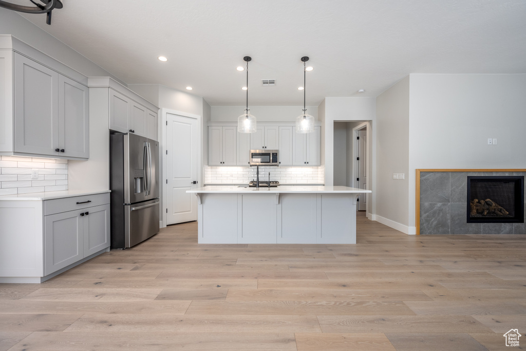 Kitchen featuring hanging light fixtures, light hardwood / wood-style floors, a kitchen island with sink, and stainless steel appliances