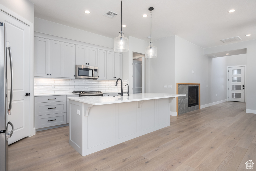 Kitchen featuring a kitchen island with sink, pendant lighting, stainless steel appliances, and light hardwood / wood-style flooring