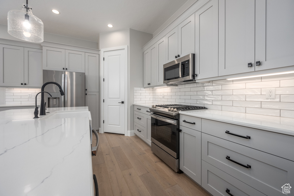 Kitchen with appliances with stainless steel finishes, backsplash, light stone countertops, pendant lighting, and light wood-type flooring