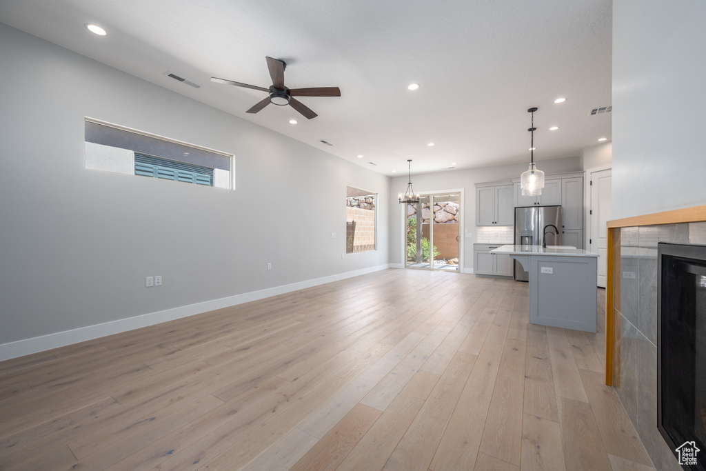 Unfurnished living room with beverage cooler, ceiling fan with notable chandelier, and light wood-type flooring