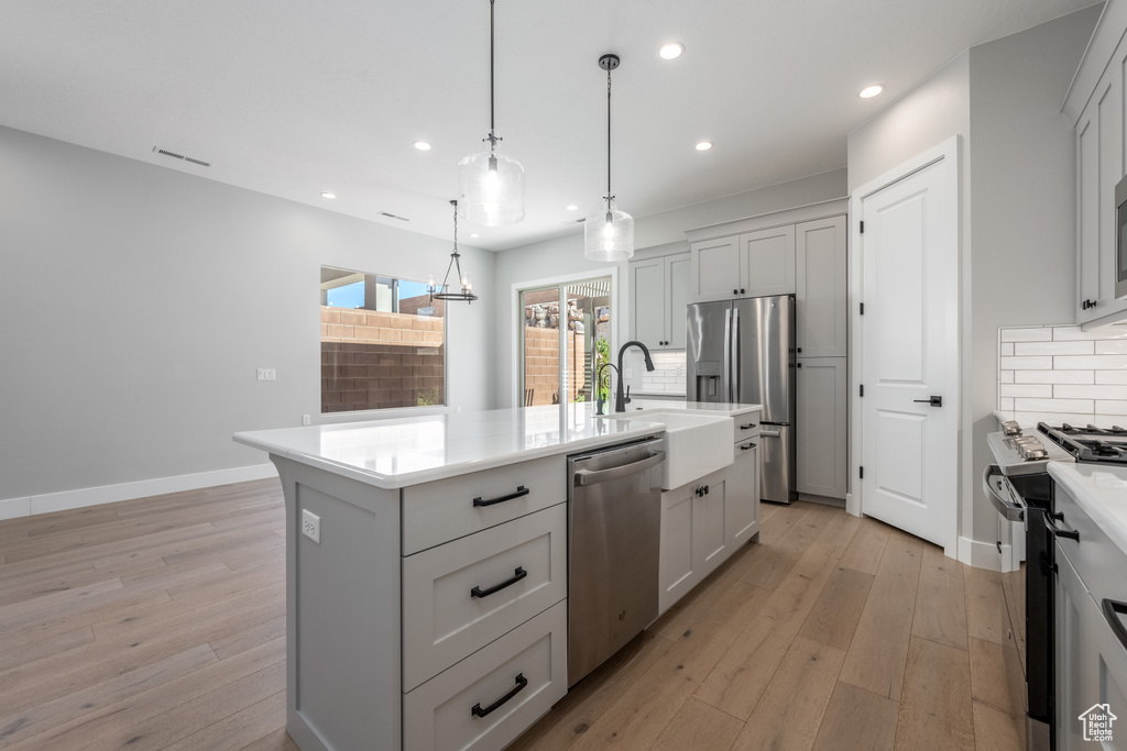 Kitchen with pendant lighting, an island with sink, decorative backsplash, light hardwood / wood-style flooring, and appliances with stainless steel finishes