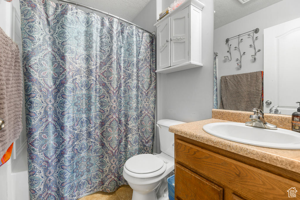 Bathroom featuring a textured ceiling, curtained shower, vanity, and toilet