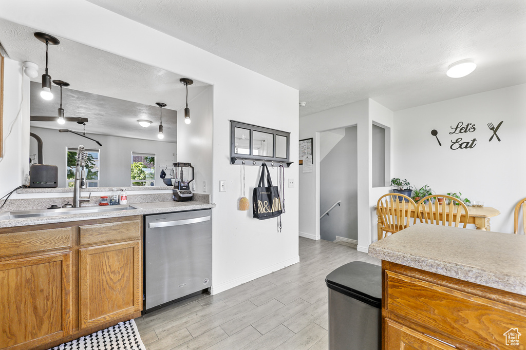 Kitchen with sink, stainless steel dishwasher, a textured ceiling, decorative light fixtures, and light hardwood / wood-style floors