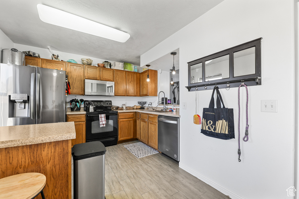 Kitchen with pendant lighting, light wood-type flooring, sink, kitchen peninsula, and stainless steel appliances