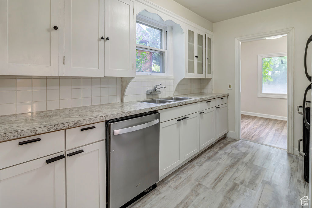 Kitchen featuring light wood-type flooring, dishwasher, sink, white cabinetry, and backsplash