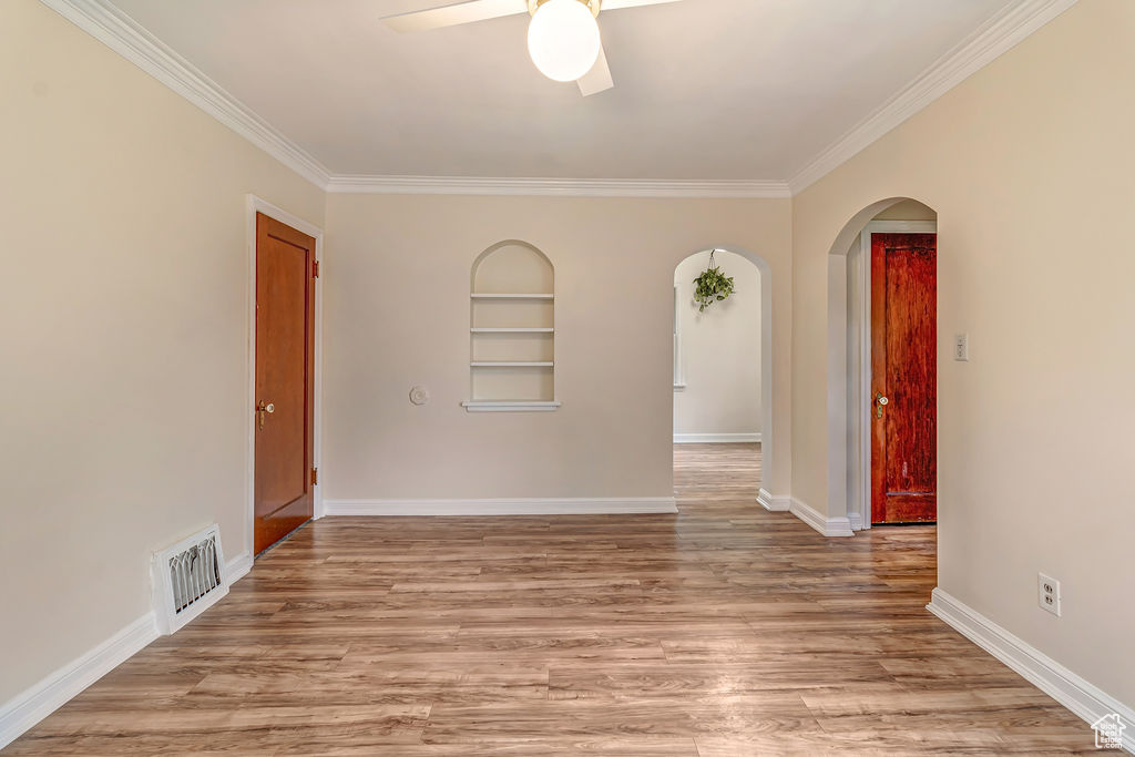 Spare room featuring ceiling fan, crown molding, light hardwood / wood-style floors, and built in shelves