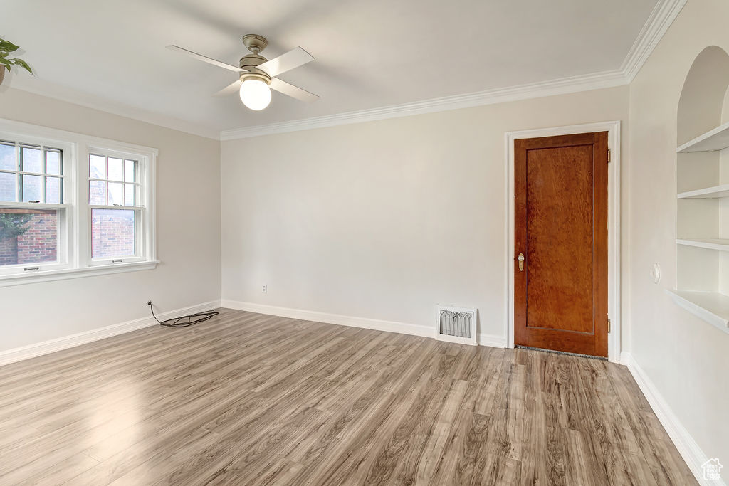 Empty room featuring ceiling fan, crown molding, light hardwood / wood-style floors, and built in features