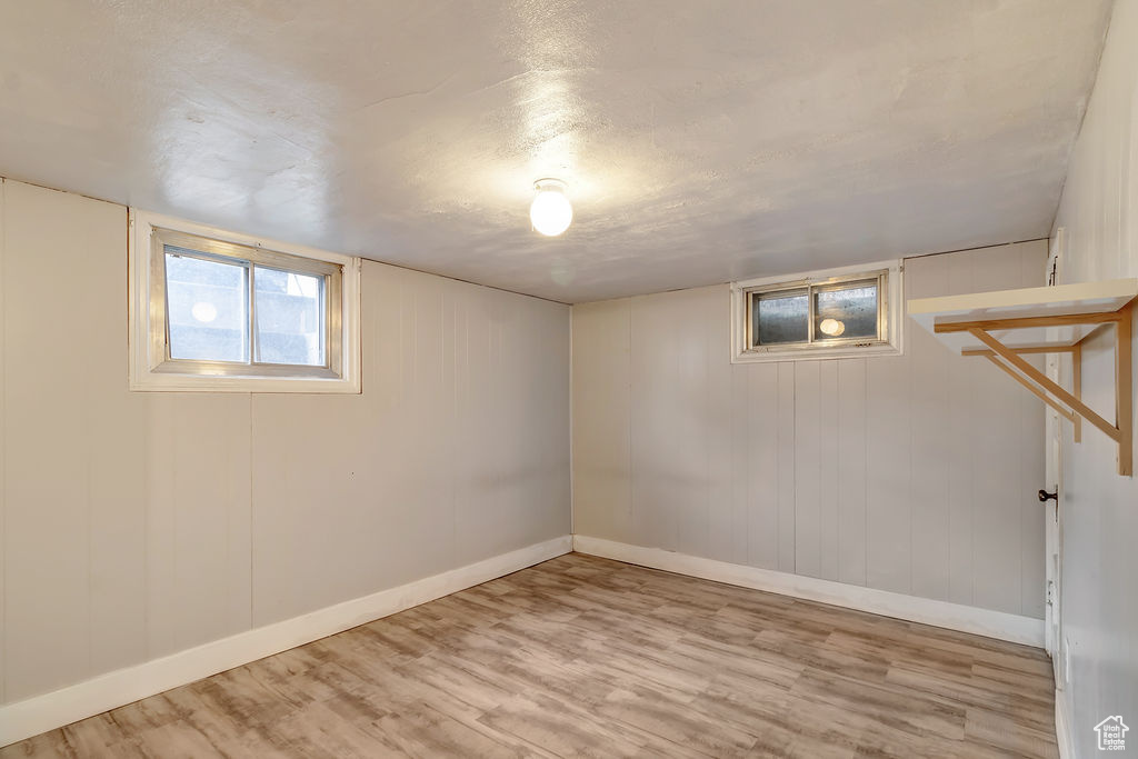 Basement with light hardwood / wood-style floors and wood walls